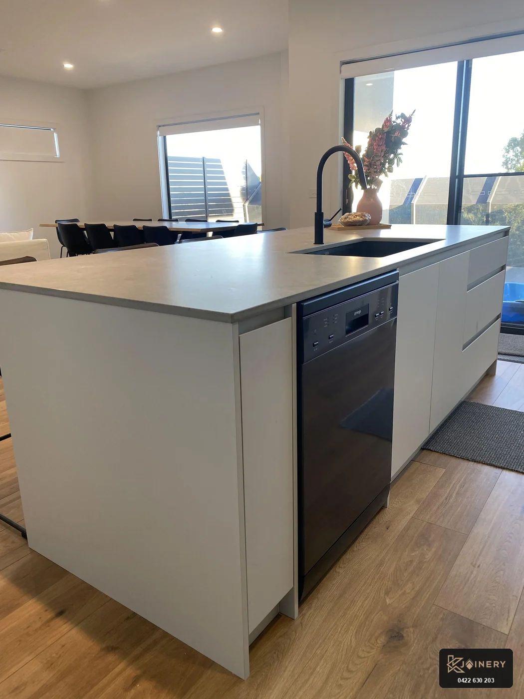 Working side of kitchen island showing shark-nose finger-pull pot drawers and integrated black dishwasher in Altona home
