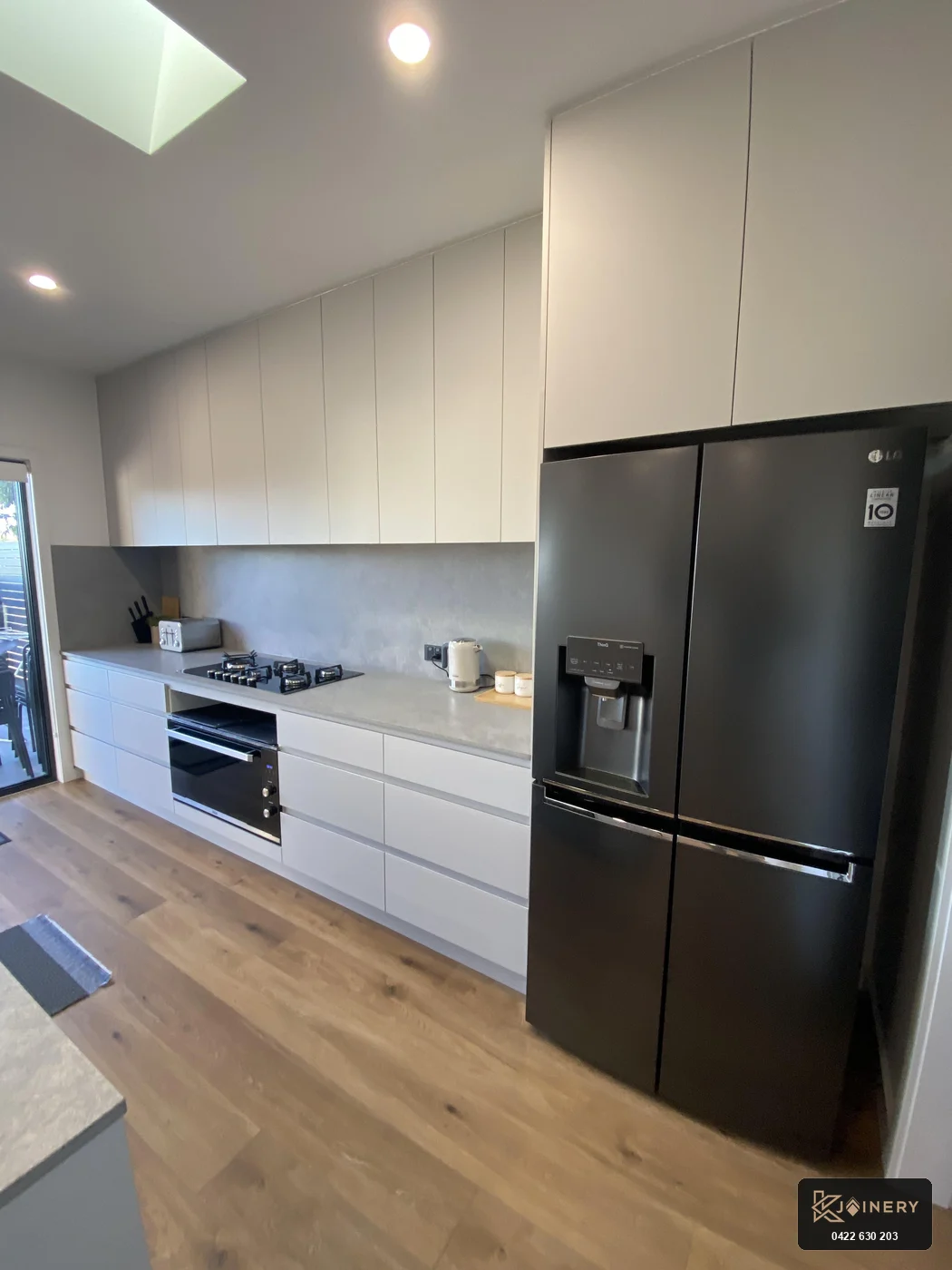 Rear wall of custom kitchen joinery in Altona featuring gas cooktop, oven and matte black refrigerator enclosure