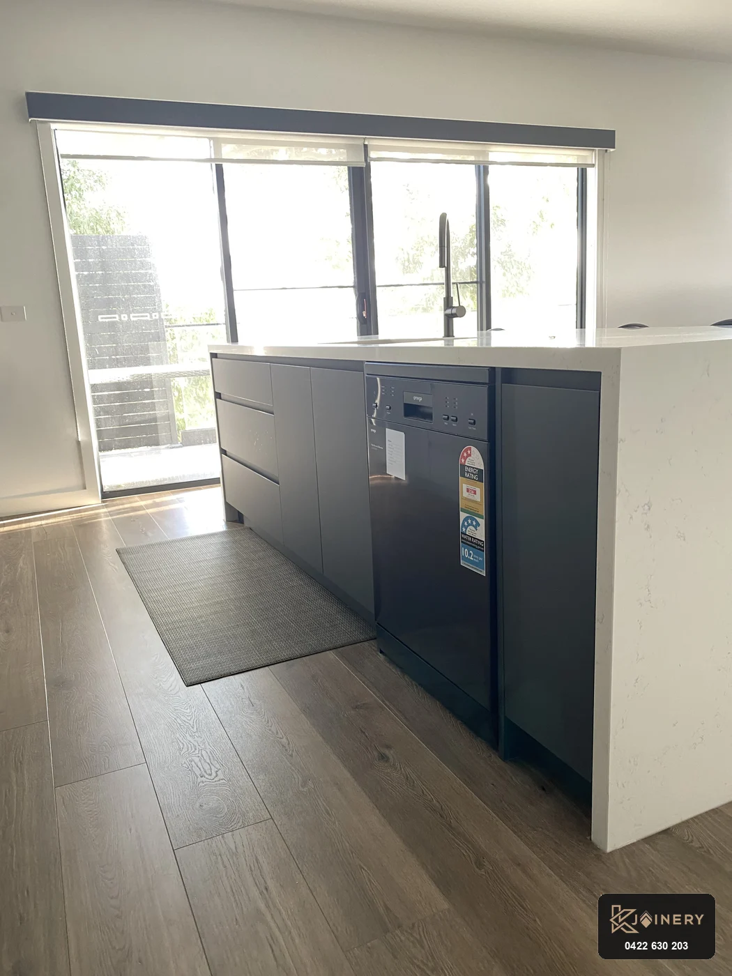 Working side of kitchen island showing shark-nose finger-pull pot drawers and integrated black dishwasher