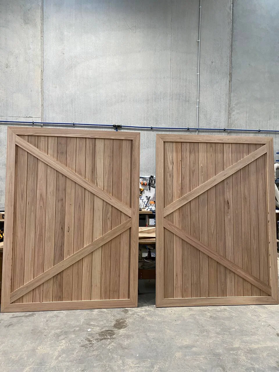 Pair of custom timber barn doors standing side by side in Ravenhall factory workshop showing mirrored chevron cross-braces